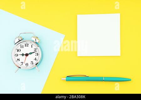 Metal vintage alarm clock with office pen and yellow sticky notes on colorful paper background Stock Photo