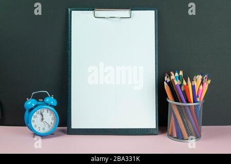Tablet with white sheet a4 next to a glass with colored pencils and blue alarm clock Stock Photo