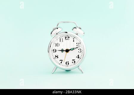 Metal vintage alarm clock on fresh pastel blue paper background. Front view Stock Photo