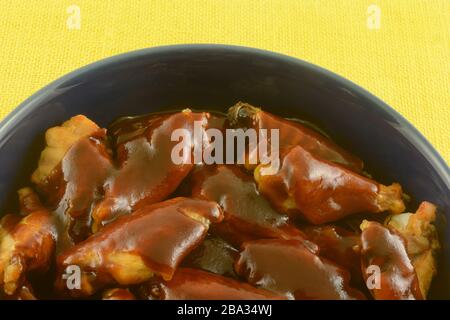 Close up of chicken wings with barbecue sauce in blue bowl against yellow tablecloth Stock Photo