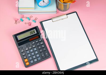 On the pink table there is a calculator and a tablet with a white sheet, next to sprinkled clothespins for paper Stock Photo