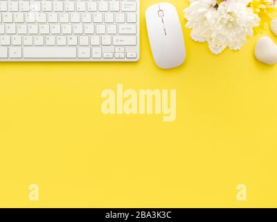 Keyboard and mouse, peony flowers and stones isolated on a yellow background. Flat lay, top view copy space. Feminine workplace concept. Stock Photo
