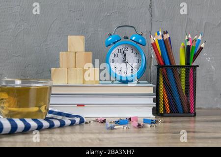 A stack of books, a clock, wooden cubes in the shape of a pyramid, next to there is tea with lemon in a transparent glass glass and multi-colored Stock Photo