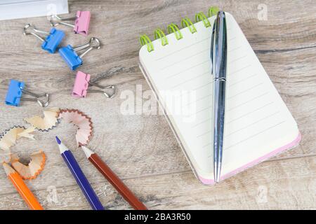 The notebook on which there is a pen of silver and next to pencil sharpening shavings and a few pencils on a wooden table Stock Photo