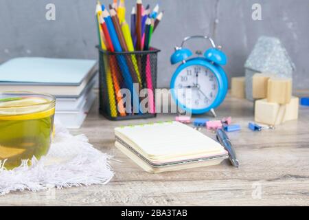 A stack of books, a clock, wooden cubes in the shape of a pyramid, next to there is tea with lemon in a transparent glass glass and multi-colored Stock Photo
