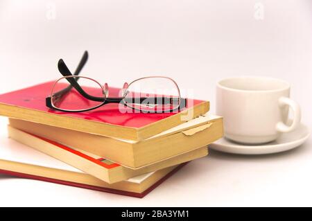 Image of some books on which there are reading glasses next to an infusion cup all isolated on white background Stock Photo