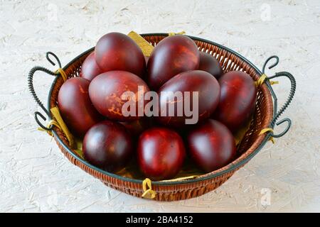 Lot of Easter eggs naturaly painted by onion shells in a wicker basket over wooden white background, side and above view Stock Photo