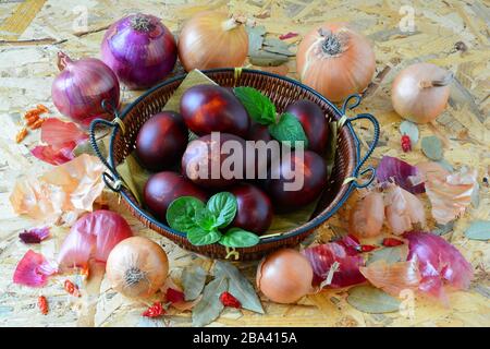 Easter eggs in wicker basket and yellow and red onion, peppers and green basil and lemon balm leaves on wooden background, angle view Stock Photo