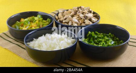 Chopped fresh raw bell peppers, poblano peppers, mushrooms and onion in blue bowls as ingredients for making dinner Stock Photo