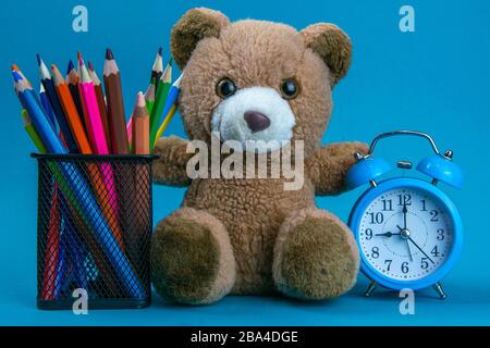 Blue alarm clock with brown bear and colorful pencil placed on the wooden table. Time to work. Use for background and texture Stock Photo