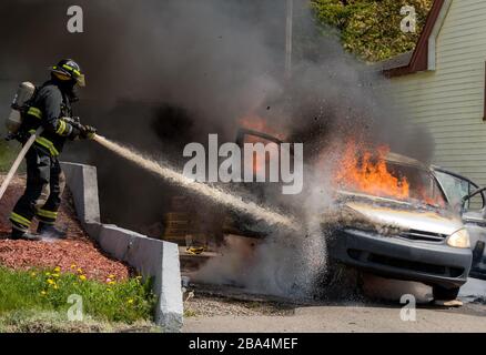 A fireman fighting the fire in a car. He is spraying the car with a hose, and wearing an oxygen tank and mask. Fire in the window Black smoke. Stock Photo