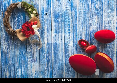 Easter decorative wreath with small and big red eggs on a blue wooden surface Stock Photo
