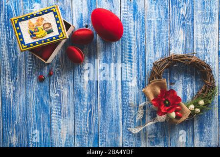 Easter background with red eggs, decorative wreath and a bunny box full of eggs on a light blue painted wooden board Stock Photo