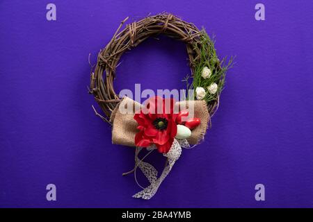 An easter decorative wreath with a flower, eggs and a ribbon on a dark purple surface Stock Photo