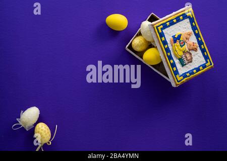 Dark purple background with an easter bunny box full of yellow and white plastic fake decorative eggs Stock Photo