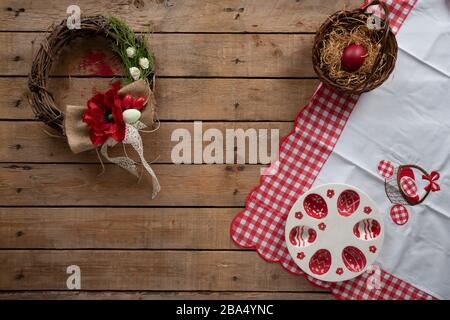 Easter decoration on a wooden surface with tablecloth, nest with a red egg, decorative wreath and a plate for easter eggs Stock Photo