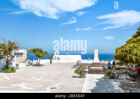 A young woman poses atop a white wall overlooking the Ionian Sea on a summer day in Oia, Santorini, Greece. Stock Photo