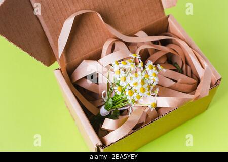 Spring composition. Cardboard box with flowers and ribbon on a bright green background Stock Photo