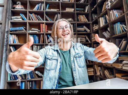 Young bearded smiling student blogger look at camera thumbs up. Stock Photo