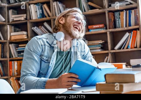 Positive overjoyed student at library burst out laughing hold book. Stock Photo