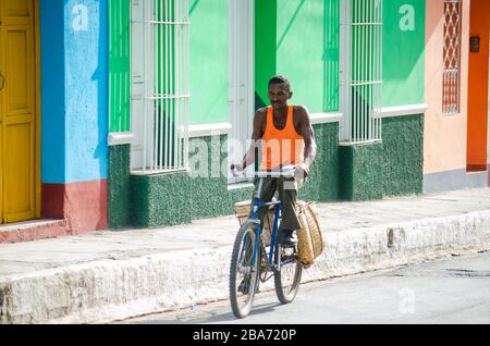 A man riding a bike through the streets of Trinidad in Cuba, carrying a palm straw shopping bag as is accustomed Stock Photo