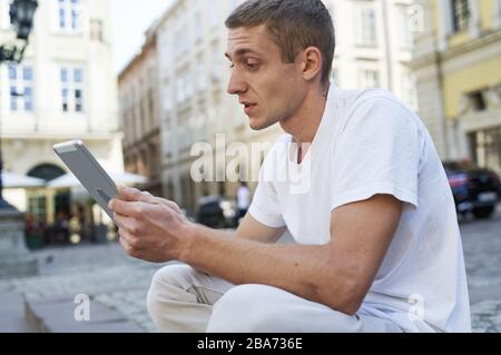 man sitting on the sidewalk uses a tablet Stock Photo