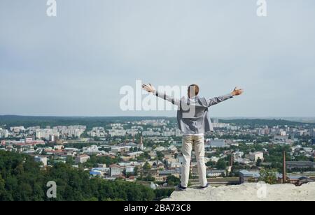 portrait of young happy businessman on top of rock. his arms are open, he loves the world Stock Photo