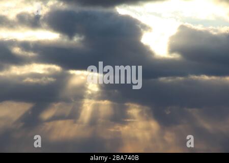 The sun at sunset or dawn behind the clouds, shines through. The sun's rays in the sky. Stock Photo