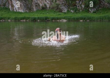 Mature caucasian man holding waterproof camera and swimming in river, trying to catch some interesting shots. Professional photographer job concept. W Stock Photo