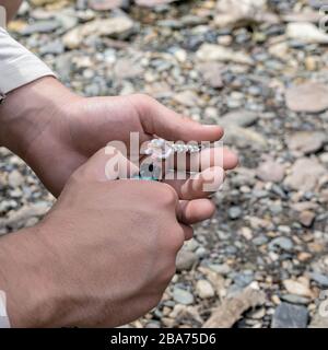 Macro shot of hands of man holding metallic lighter and cord just in moment of setting on fire. Blurry background, copy space. second before light is Stock Photo