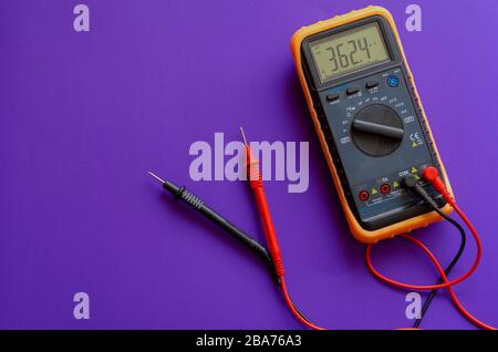 Multimeter on a lilac background. Yellow Multimeter, A multimeter or a multitester is an electronic measuring instrument. A typical multimeter can mea Stock Photo