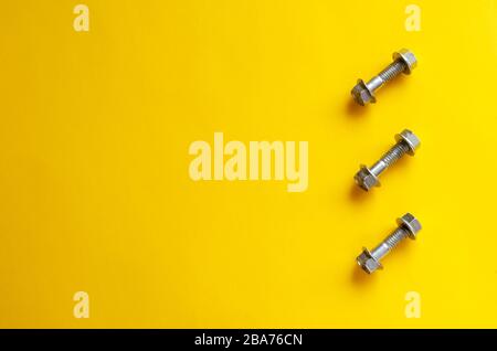Nuts and bolts on a yellow background. Composition and three bolts with nuts. Free space on the left. Abstract multitask background. View from above.