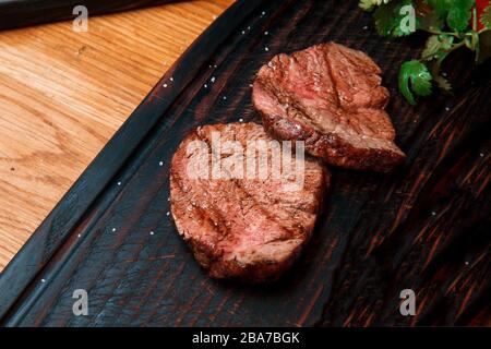 Thick juicy portions of fried fillet steak are served, sprinkled with salt, on an old wooden board. The dish is ready to serve. Stock Photo