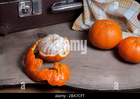 Several of whole fresh orange mandarine or oranges, tangerines, clementines, citrus fruits and one fruit is half peeled on wooden board Stock Photo