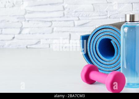 Pink dumbbells, bottle of isotonic drink and fitness mat on white