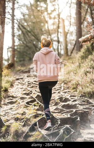 Rear view of active sporty woman listening to the music while running in autumn fall forest. Female runner training outdoor. Healthy lifestyle image