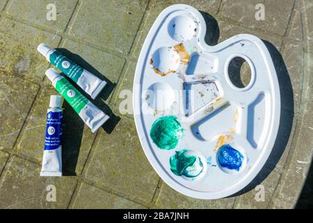 Tubes of acrylic paint and an artist's palette on an outdoor table. Stock Photo