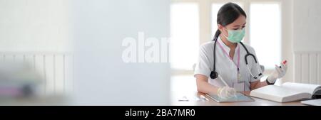 Cropped shot of female doctor analysing test tube and looking for Information in a Medical Book while sitting in examination room Stock Photo