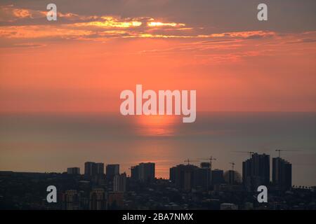 Stunning view of the setting sunlight reflection on the sea with group of skyscrapers in foreground Stock Photo