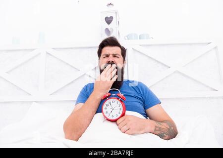 Healthy habits. Wake up early every morning. Health benefits of rising early. Waking up early gives more time to prepare and be timely. Hipster bearded man in bed with alarm clock. Time to wake up. Stock Photo