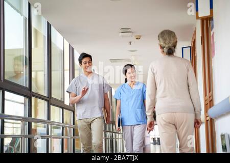 happy young asian physical therapists greeting residents in hallway of nursing home Stock Photo
