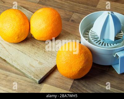 Three oranges with a chopping board and an orange squeezer on a wood block kitchen worktop Stock Photo