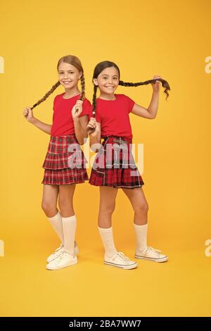 Cheerful friends. Cute little girls smiling yellow background. Happy small girls wearing same outfits. Friends enjoying friendship. Playful kids. Happy together. School friends having fun together. Stock Photo