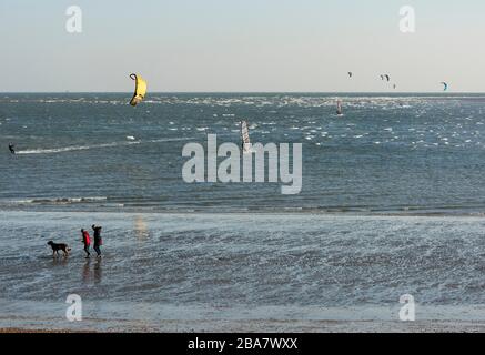 Two people walk a dog on Hayling Island with wind and kite surfersin the background the day before the UK entered into coronavirus lockdown Stock Photo