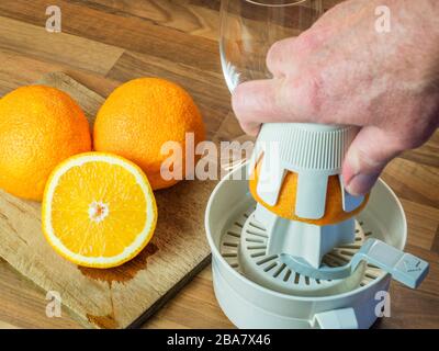 Oranges and half orange on a chopping board and a hand squeezing an orange with an orange squeezer on a wood block kitchen worktop Stock Photo