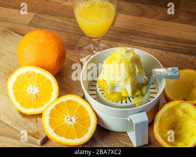 Oranges and half oranges on a chopping board with an orange squeezer and freshly squeezed oranges with a glass of orange juice on a worktop Stock Photo