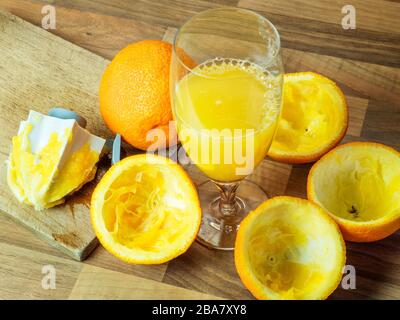 A glass of freshly squeezed orange juice with a whole orange and squeezed orange halves on a kitchen worktop Stock Photo