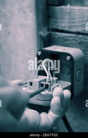 Man wiring an electric socket using an electrical screwdriver outdoor outside.  With colour toning Stock Photo
