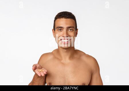 Sick African American guy eating medicine pill. Black man standing on plain background with copy space Stock Photo