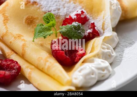 close up view of tasty crepes with raspberries and whipped cream on plate Stock Photo
